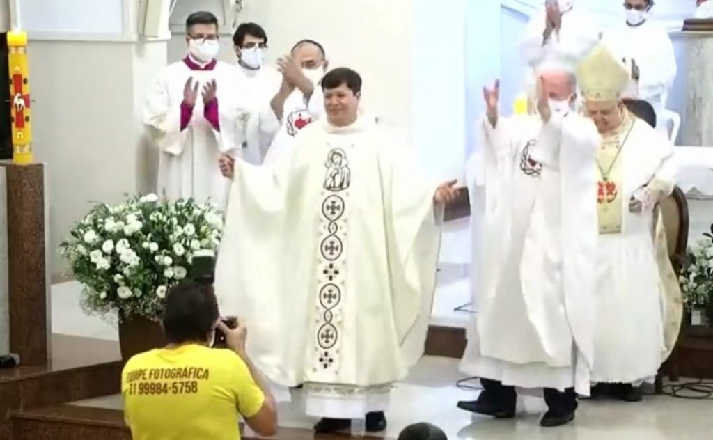 Padre armin, no altar da igreja do Padre Eustáquio, se apresentando para a comunidade como novo padre, durante sua ordenação. Sendo aplaudido e fotografado